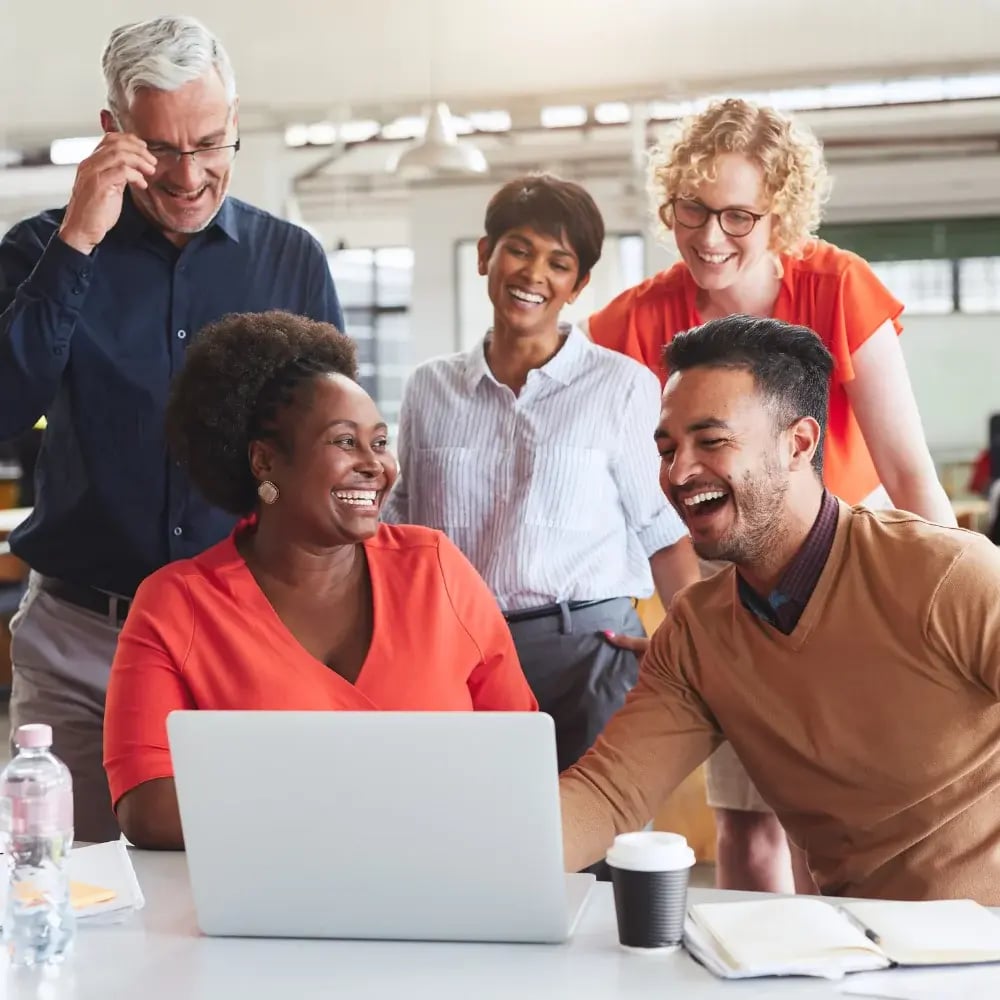 A diverse group of people gathered around a laptop in an office setting.