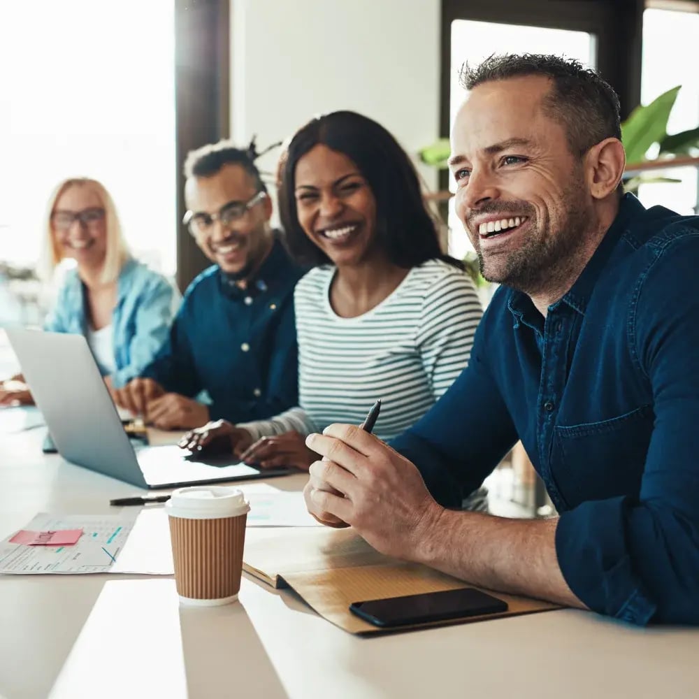 A group of diverse individuals seated at a table, each using a laptop for collaborative work or discussion
