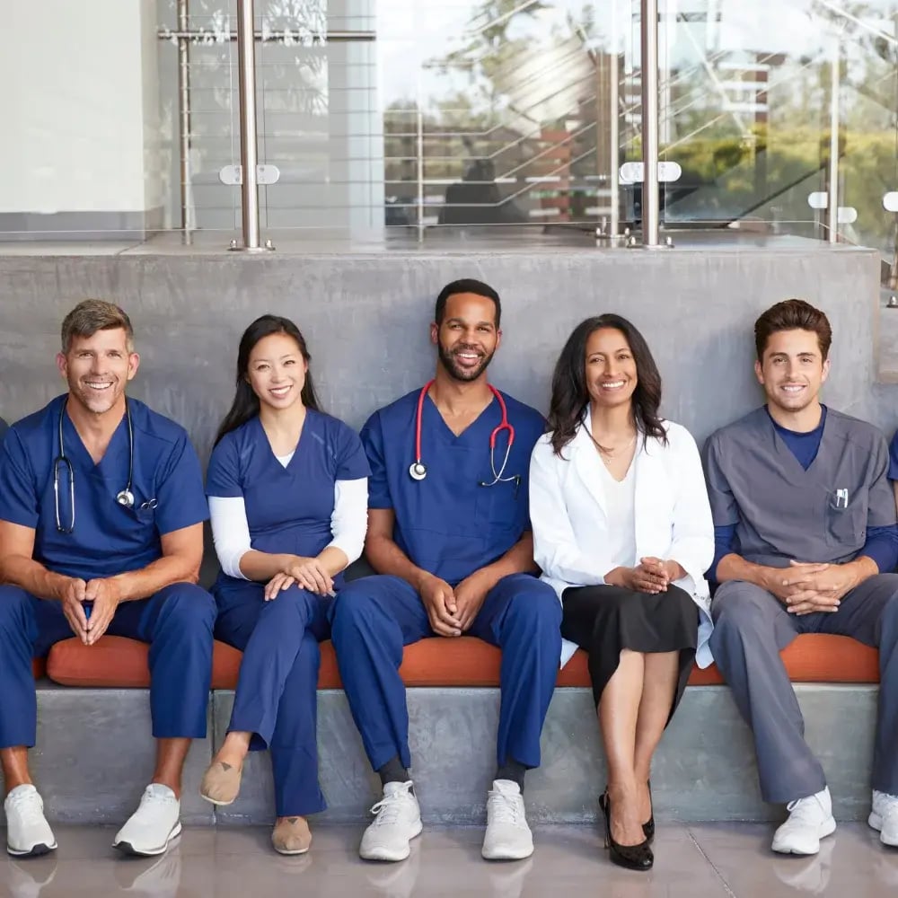 A group of medical professionals and a recruiter sit on a bench in a public space
