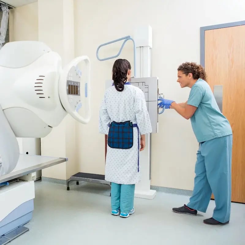 A healthcare professional in scrubs assists a patient in a medical gown for an X-ray