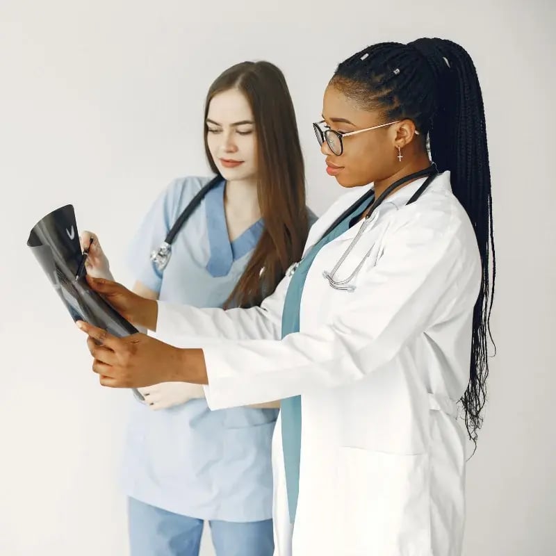 A nurse in scrubs and a physician in a lab coat, one holding an X-ray film, focused and discussing.