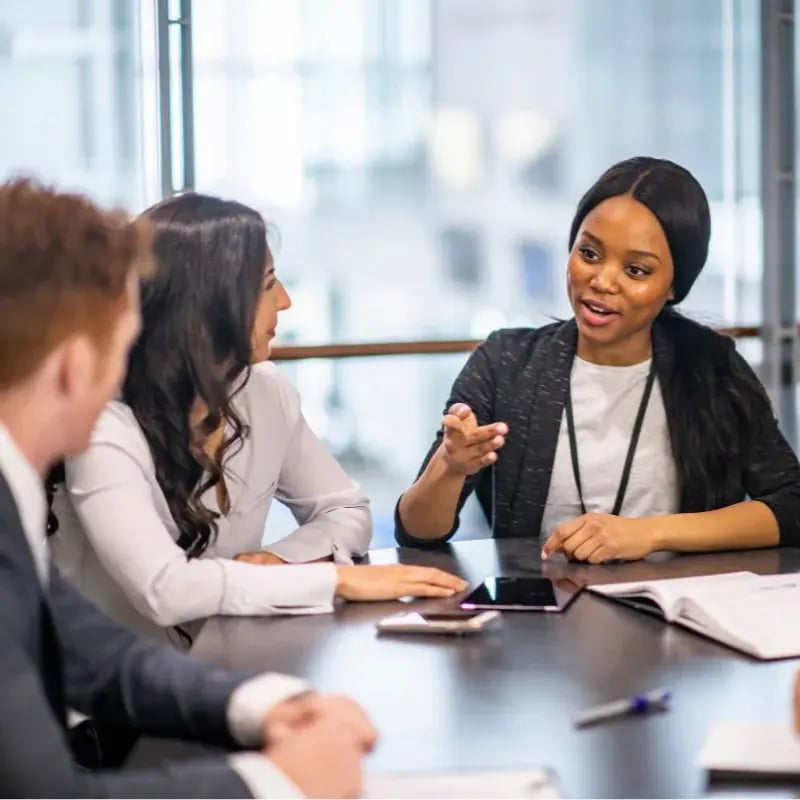 A woman in a business suit engages in conversation with her colleagues in a professional setting.