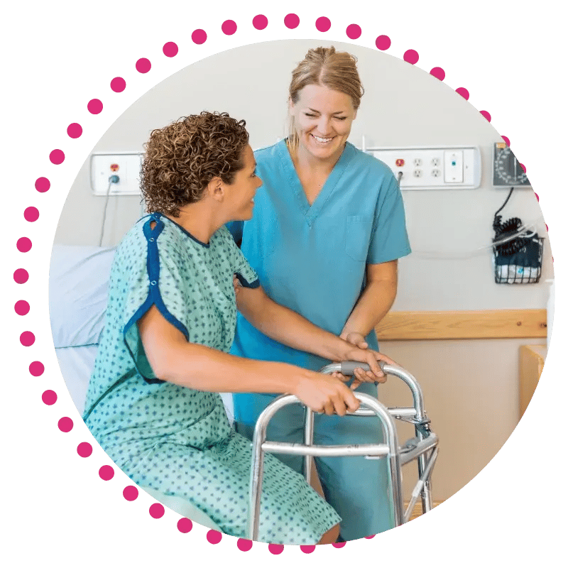 A nurse in blue scrubs assists a patient using a walker in a hospital room.