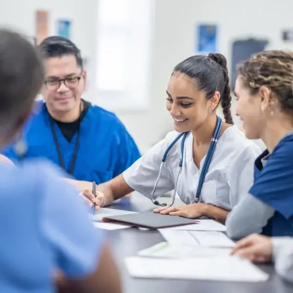One doctor writing on a paper with other 4 doctors on a meeting smiling