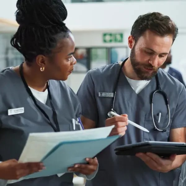 Female doctor with papers on her hand and a Male doctor looking a tablet having a conversation