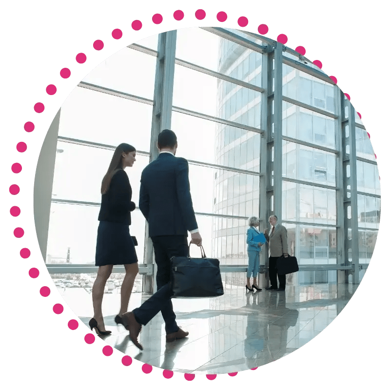 Professionals in formal attire walk through a modern, glass-walled office lobby.