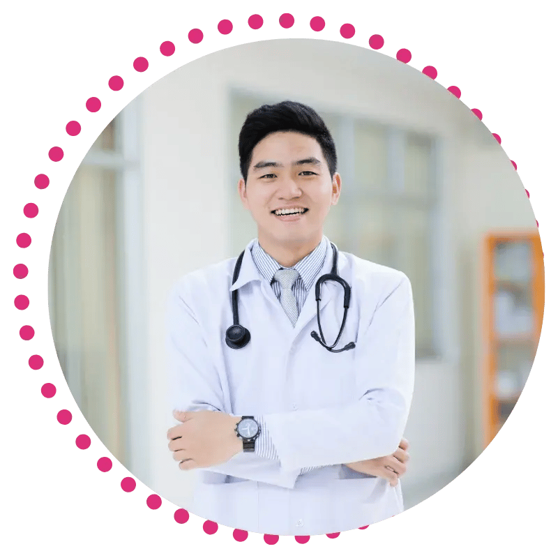 Smiling physician in a white coat with a stethoscope, standing with arms crossed. Background is a bright office. Image framed by a pink dotted circle.