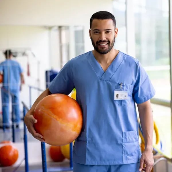 Nurse with a rehab ball smiling in front of the camera in a rehab room