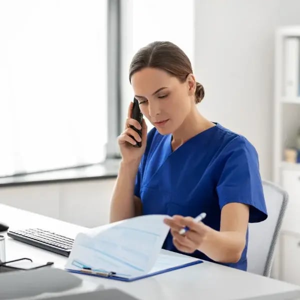 A doctor on a desktop checking papers on a table while talking on the phone