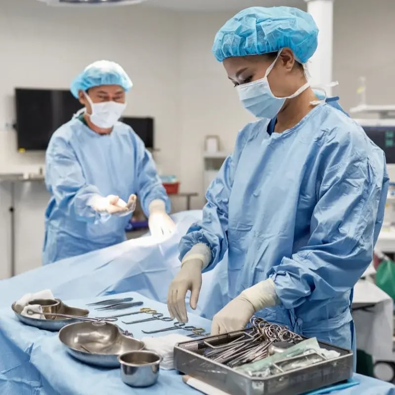 Two surgeons in blue scrubs and masks prepare instruments in an operating room.
