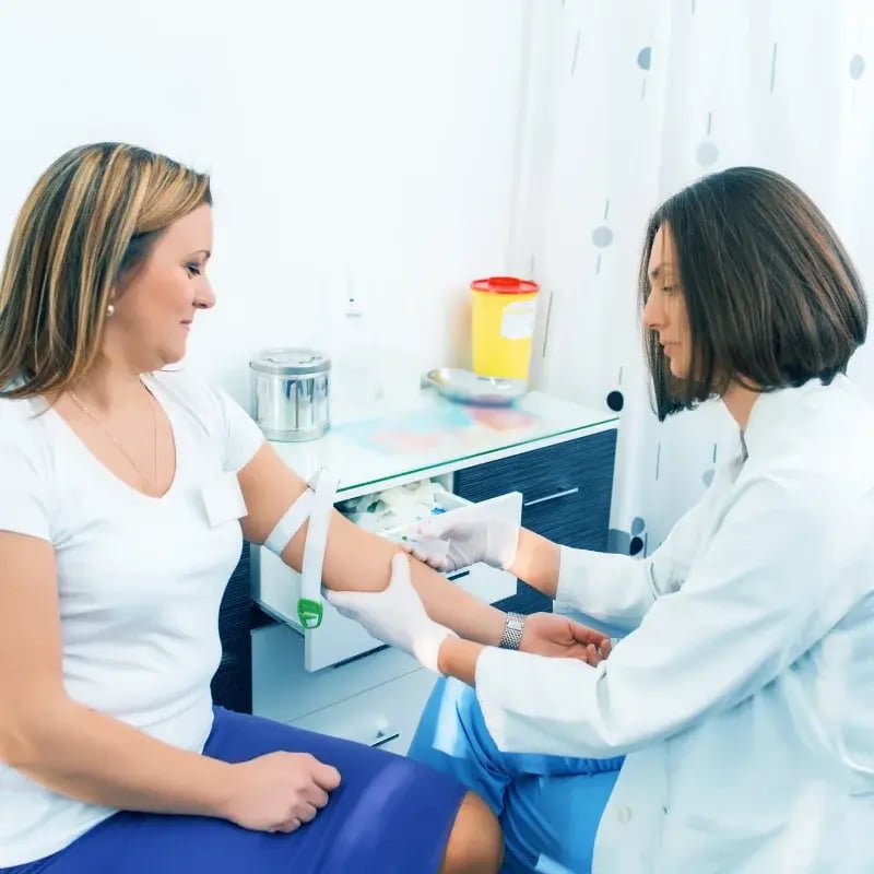 A healthcare professional draws blood from a woman’s arm in a clinic.