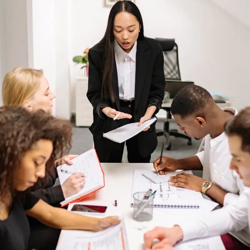 A woman dressed in a business suit stands in front of a group, engaging them with her presentation