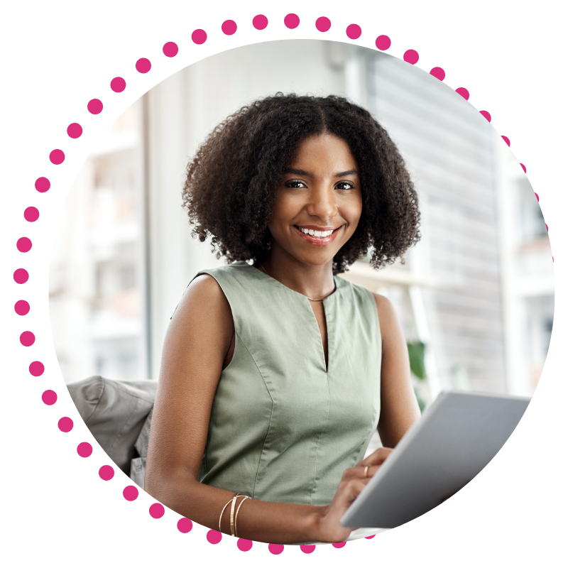 A smiling woman sits at a desk, typing on a laptop