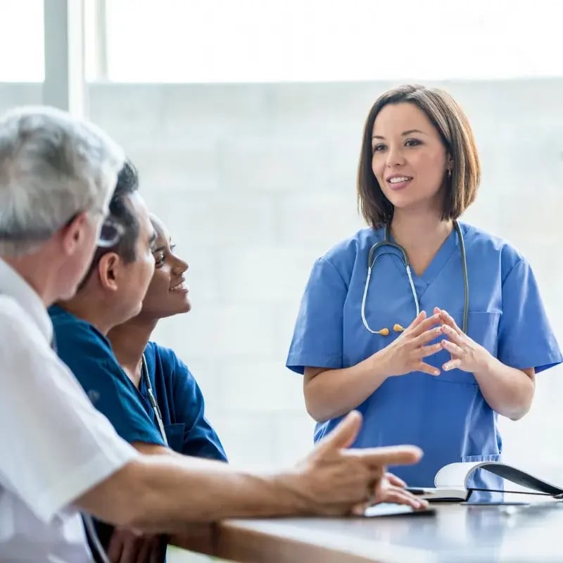 A nursing leader discussing patient care with other leaders at a table in a healthcare setting.