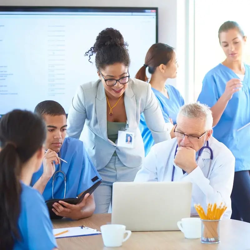 A diverse group of healthcare leaders wearing scrubs, standing together in a clinical setting.