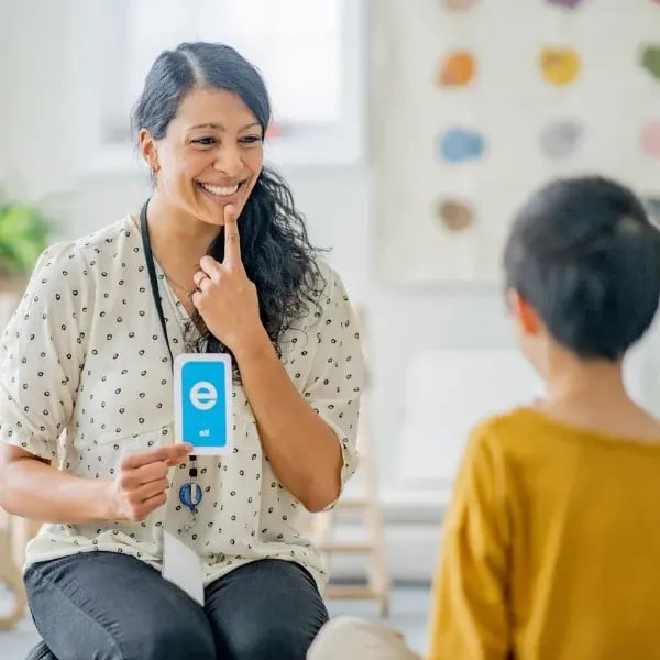 Language therapist showing an E card while putting her index finder in her chin to show language signs to a little boy