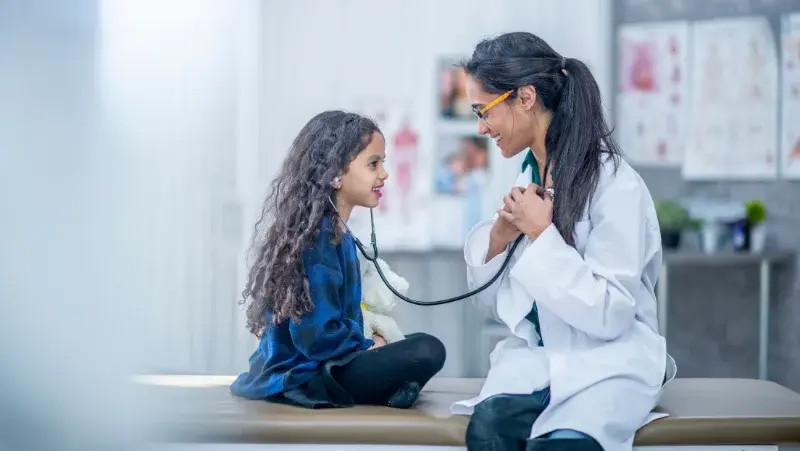 A doctor uses a stethoscope to show a little girl how to listen her heard.