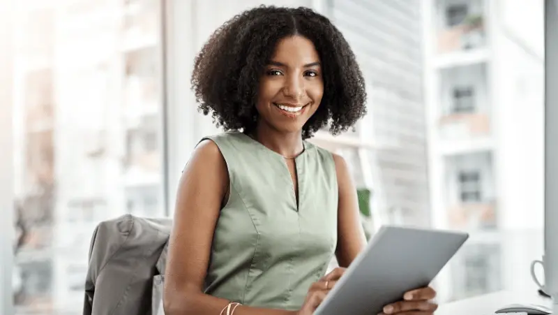 A woman on a green shirt, holding a tablet smiling.