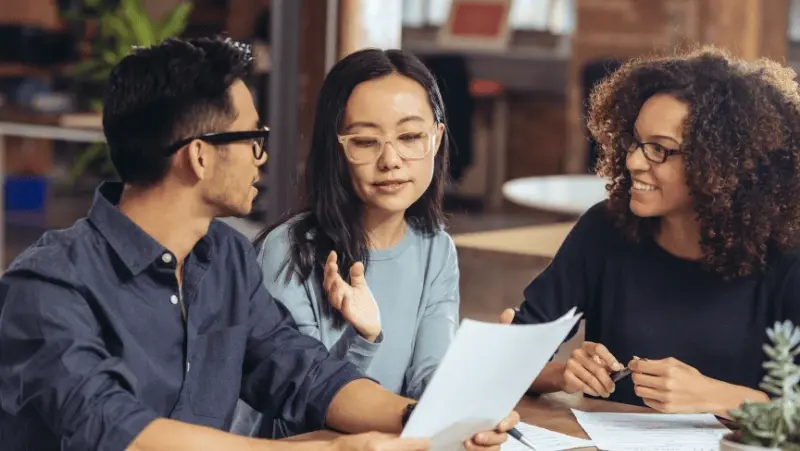 3 Persons seated talking and checking papers