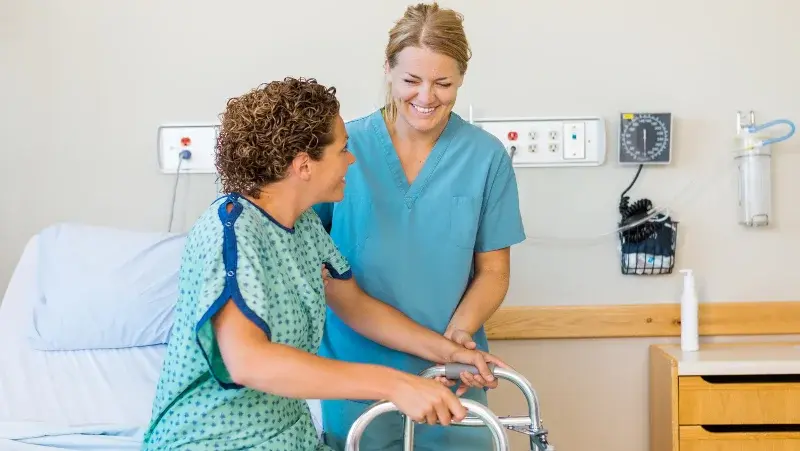Woman nurse helping a patient stand up with crutches