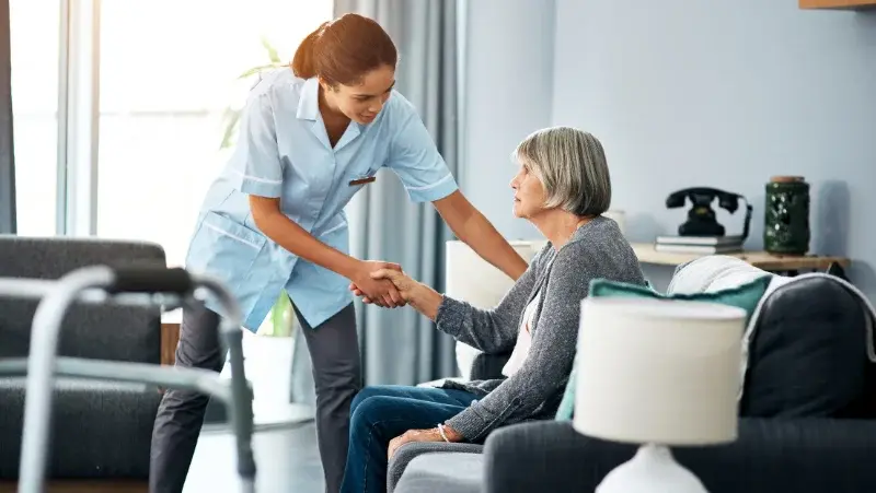 A nurse woman helping an elder to stand up by holding her hand in a nursing home